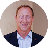 Image of an older white man wearing a black suit and blue button up