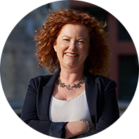 Photo of a business woman with red hair, wearing a black blazer and white blouse