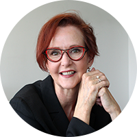 Headshot of a business woman with red hair, red glasses and a black blouse